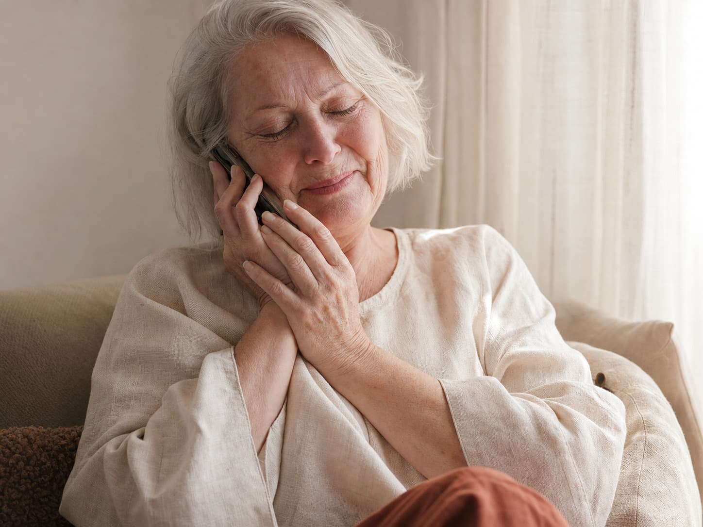 A grandmother holding a phone to her ear with both hands, eyes closed
